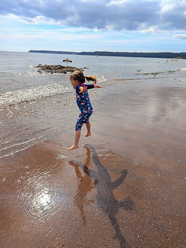 Isabella, aged 4, jumping on wet sand at the beach as the sea rolls in under her feet